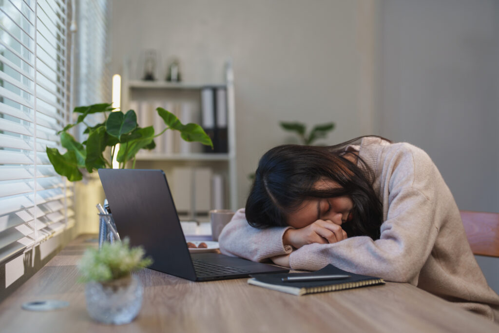 机の上にうつ伏せになって眠るアジア女性
